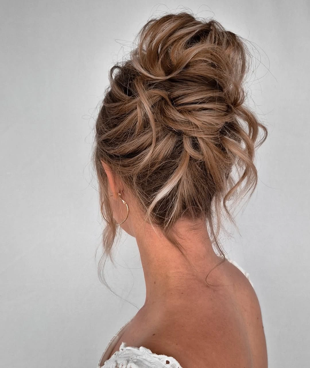 fall hairstyles for wedding guests 2026 Airy Brunette High Bun With Loose Golden Pieces