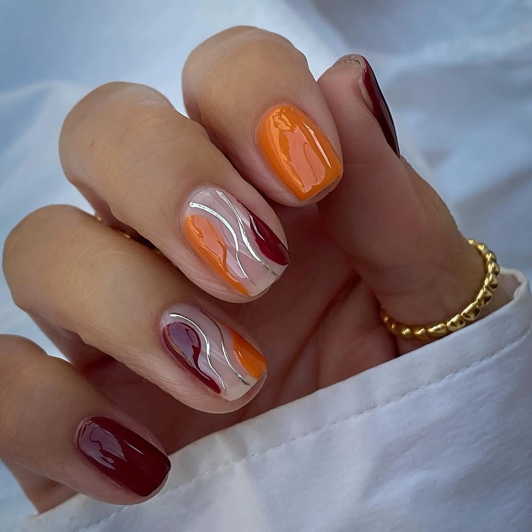Short orange and burgundy nails with a curved pale accent