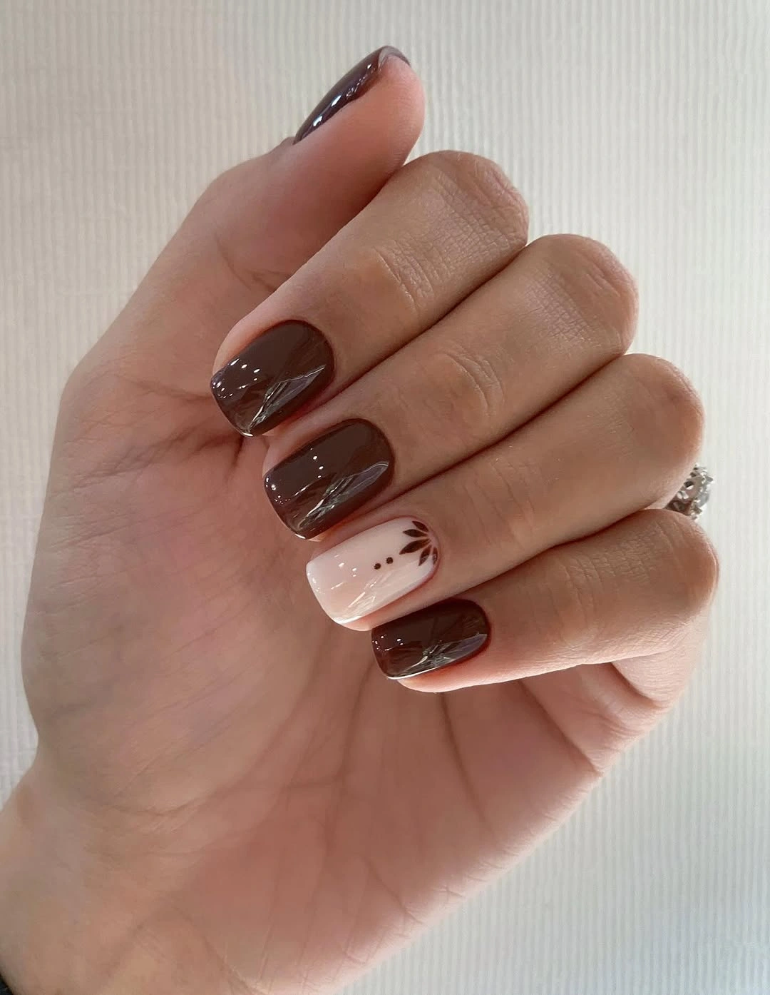 short deep brown nails with one pale leaf accent
