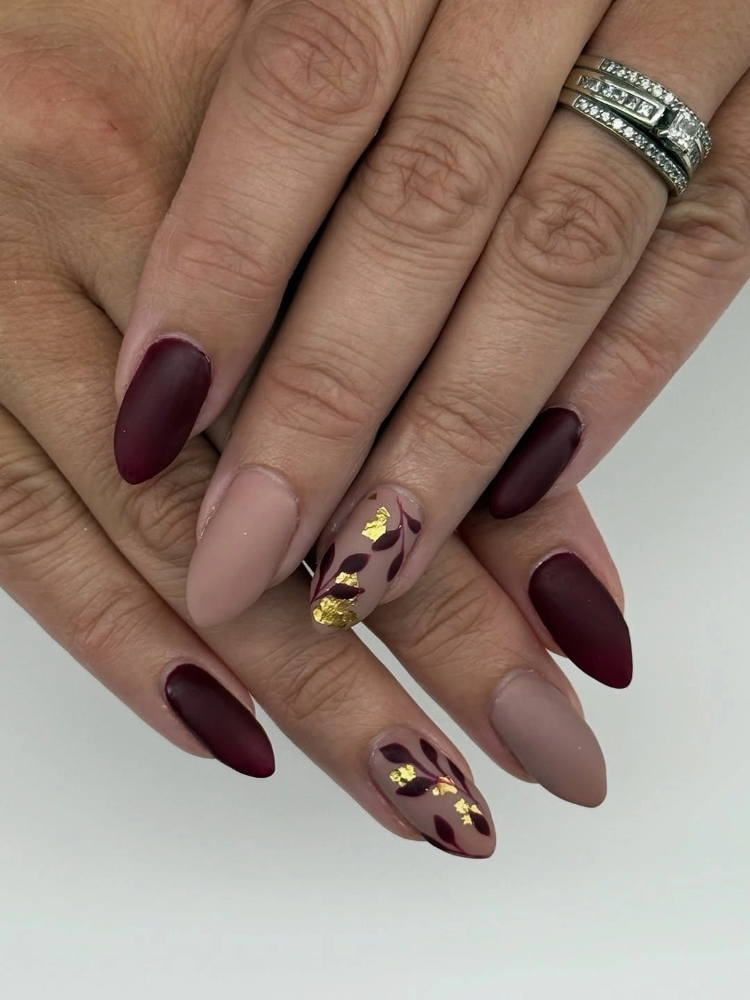 burgundy and nude almond nails with gold foil accents