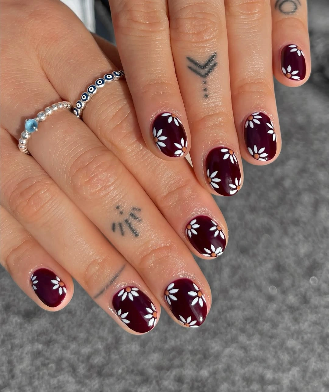short rounded burgundy nails with repeated white petal motifs