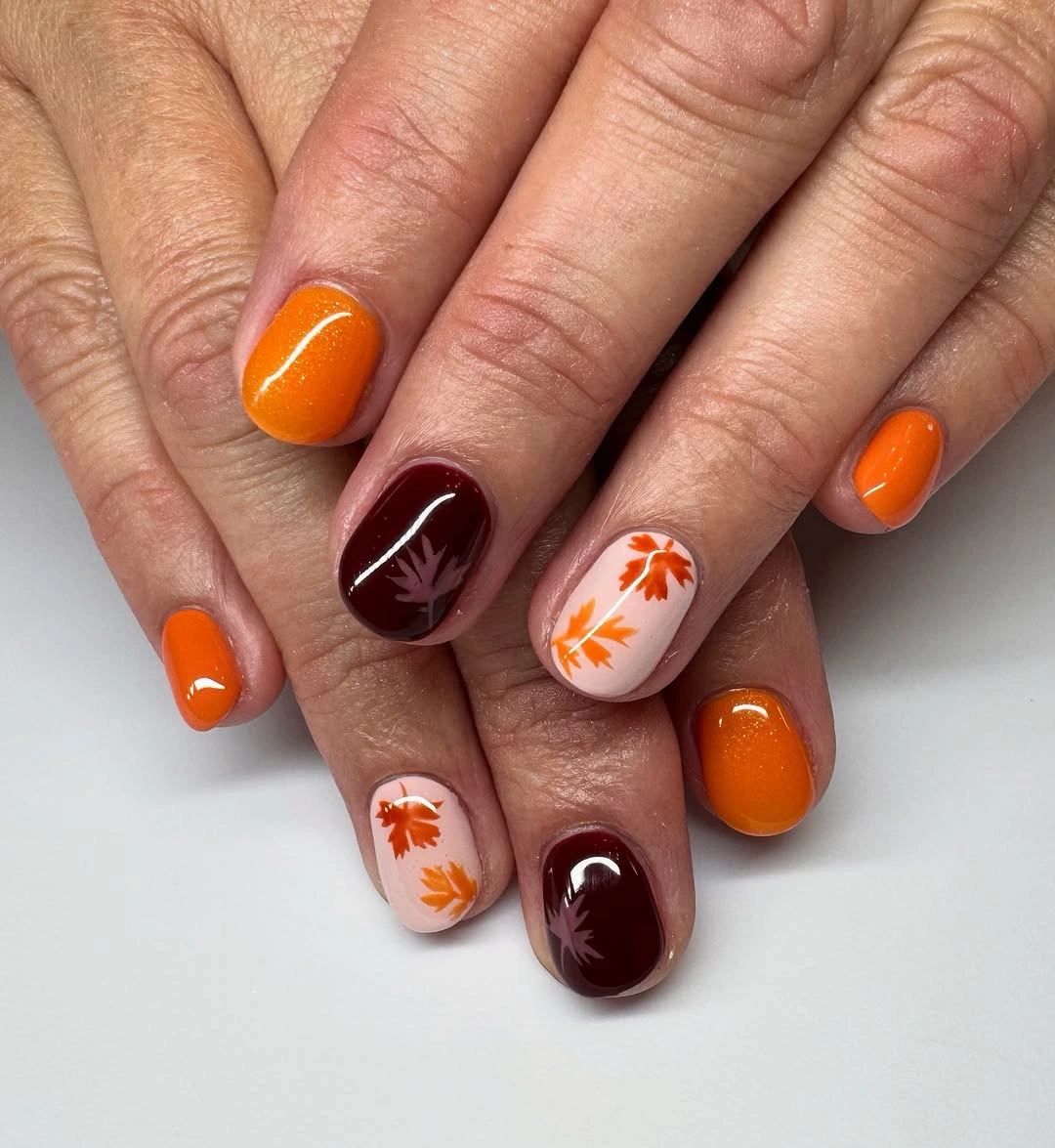 Short orange burgundy nails with cream leaf accents