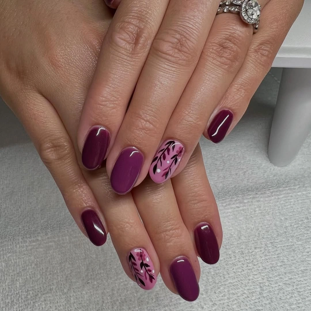 Short oval burgundy nails with one pale floral accent