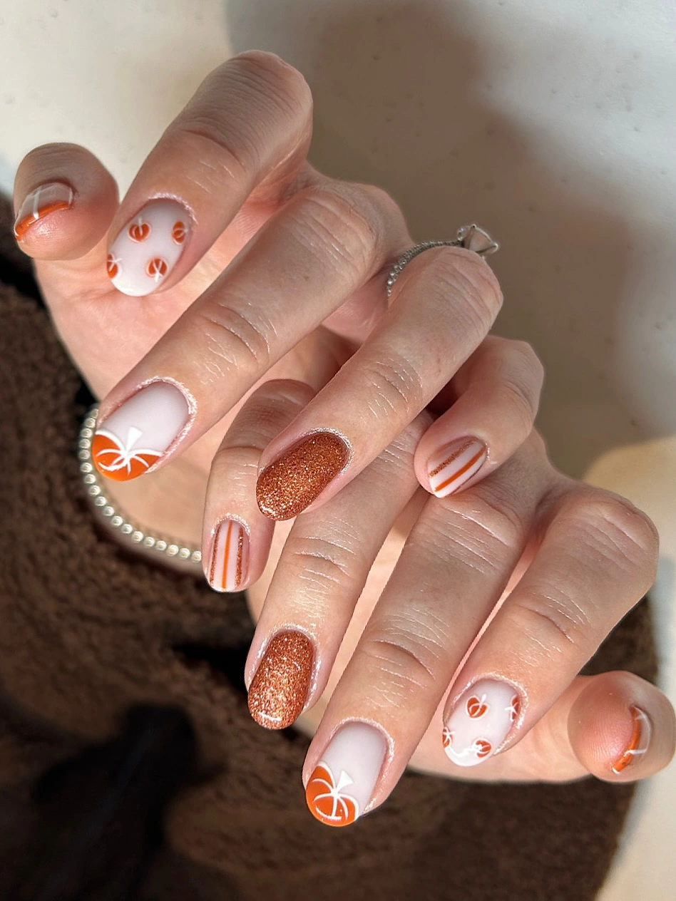 Medium square nails with pale bases pumpkins stripes and copper glitter
