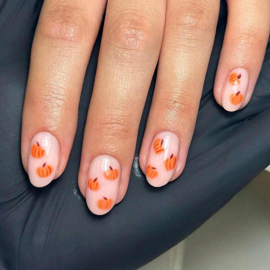 Short square pale pink nails with repeating tiny pumpkins