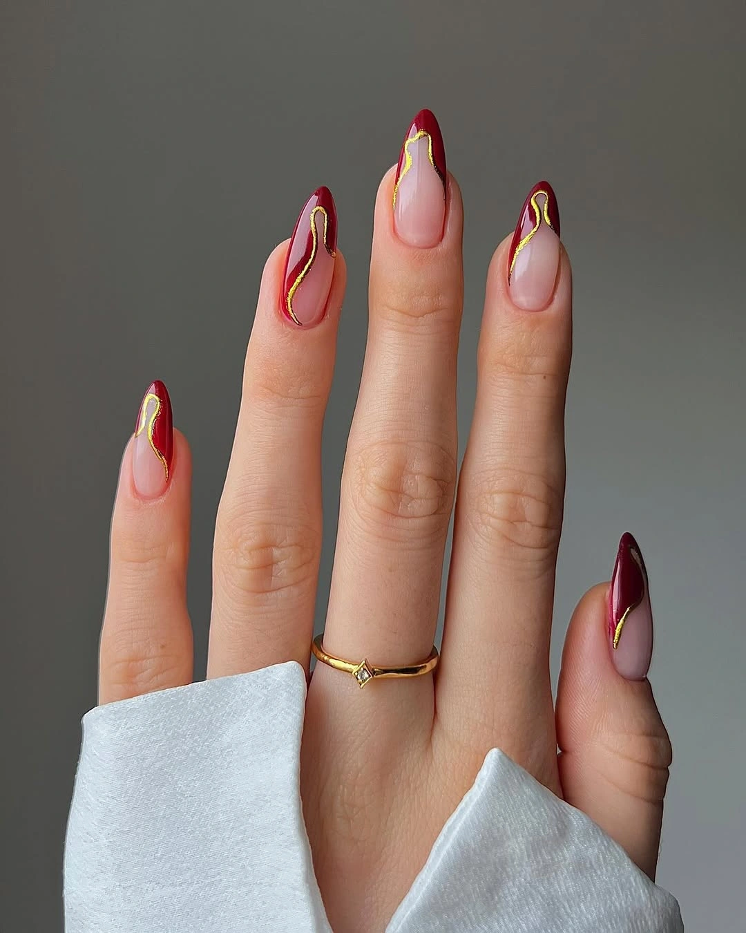 Sheer pink pointed nails with burgundy and gold curves