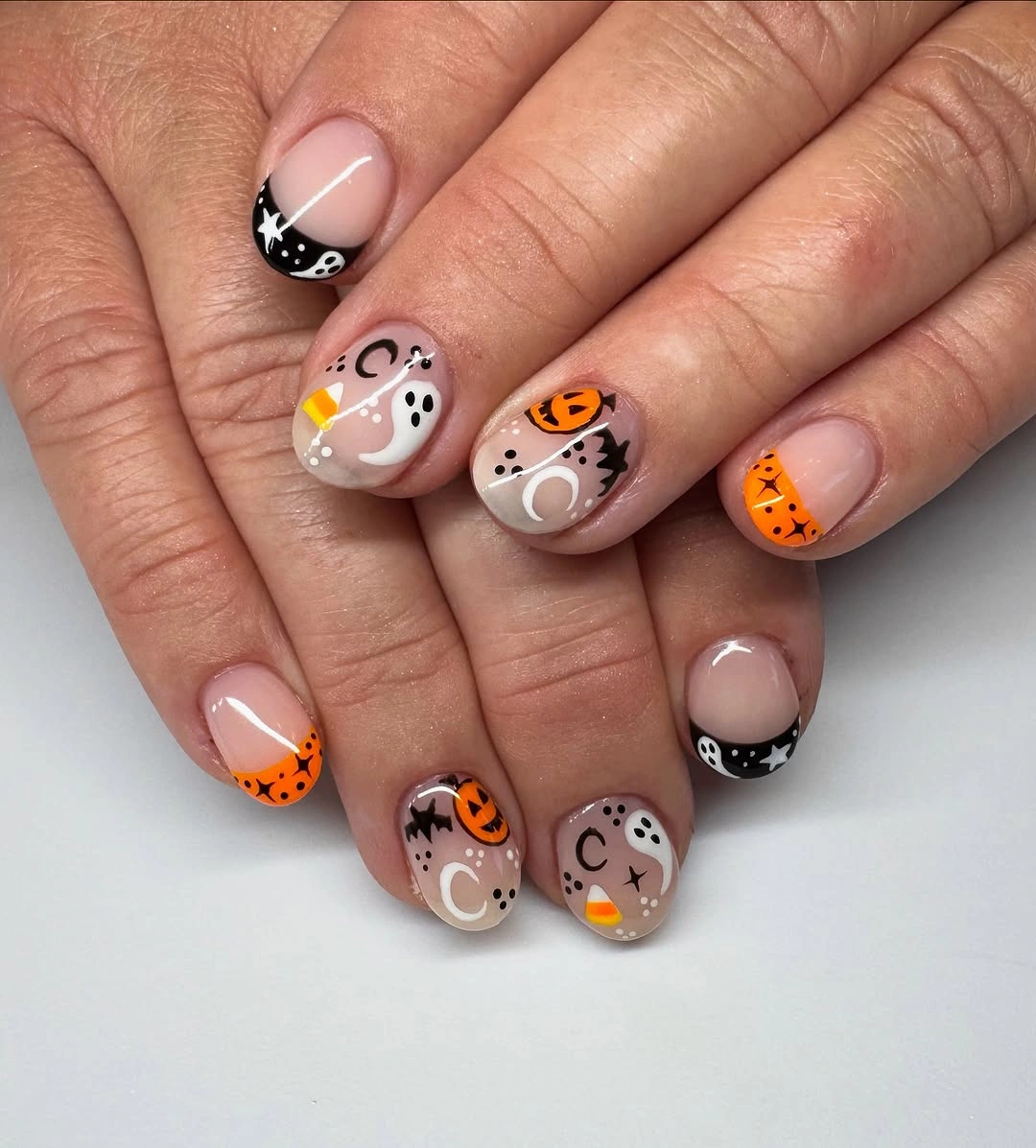 Short rounded pale nails with orange pumpkins crescents and symbols