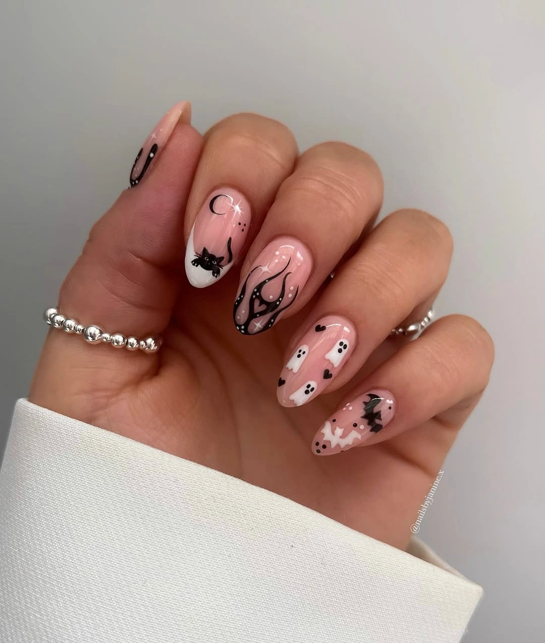 Short oval pale pink nails with black swirls and ghosts