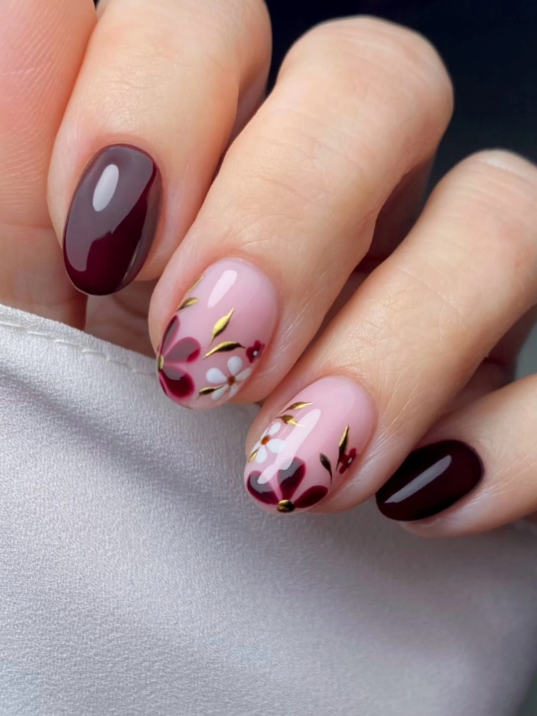 Short glossy burgundy nails with pale floral accents