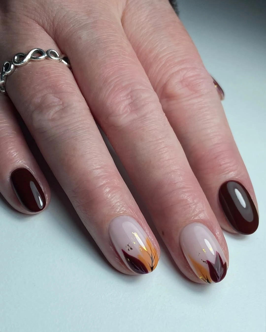 Compact burgundy nails with pale warm leaf accents