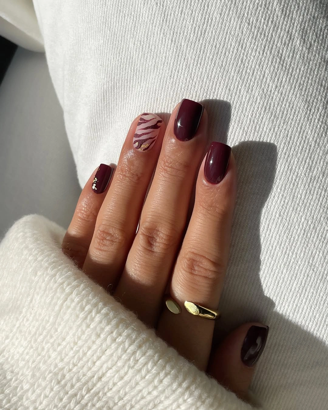 Short glossy burgundy nails with one pale leaf accent