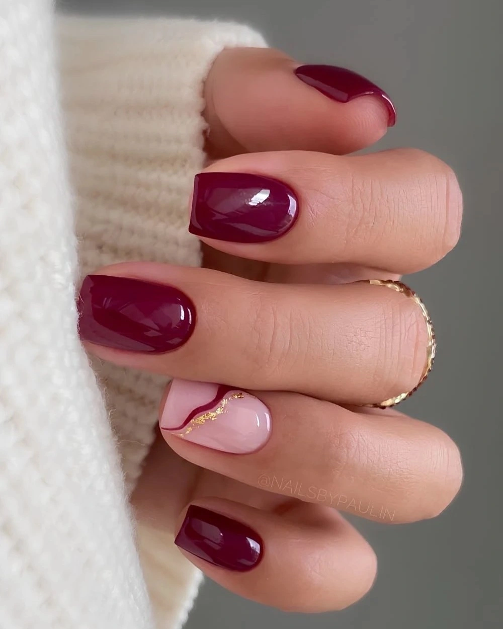 Glossy burgundy nails with one curved pink gold-edged accent