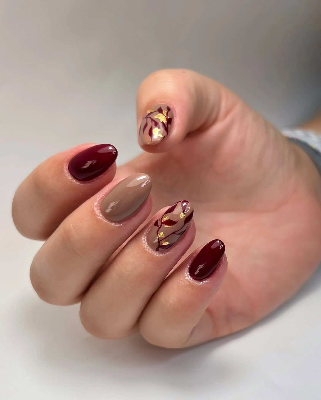 Short burgundy nails with taupe fine-line accents