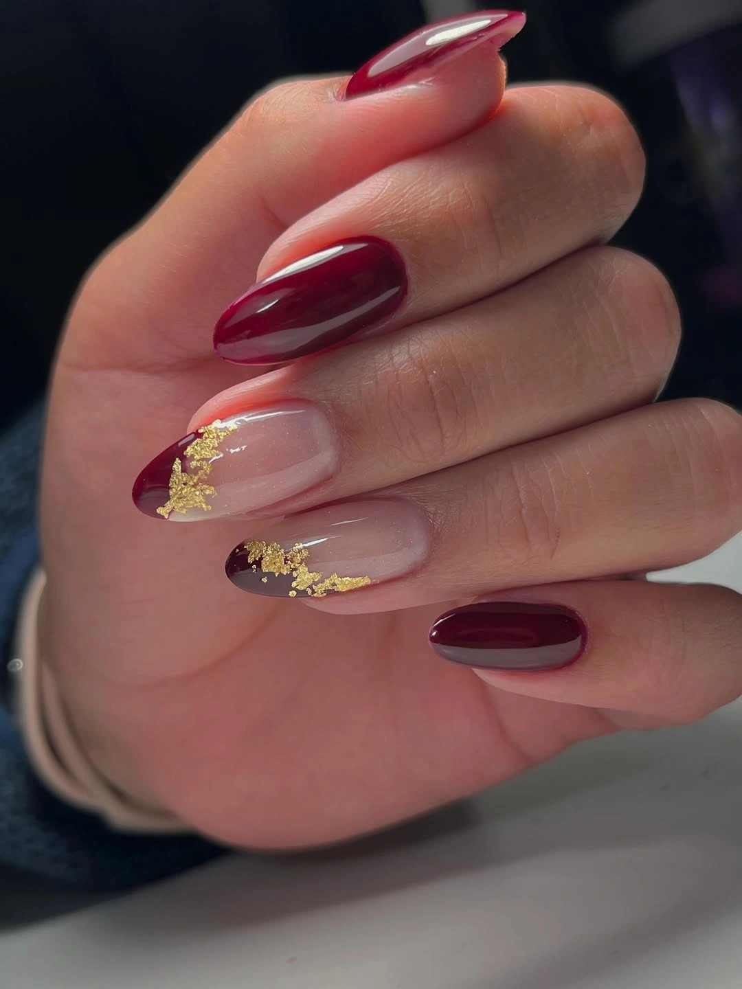 Glossy maroon almond nails with pale centers and gold accents