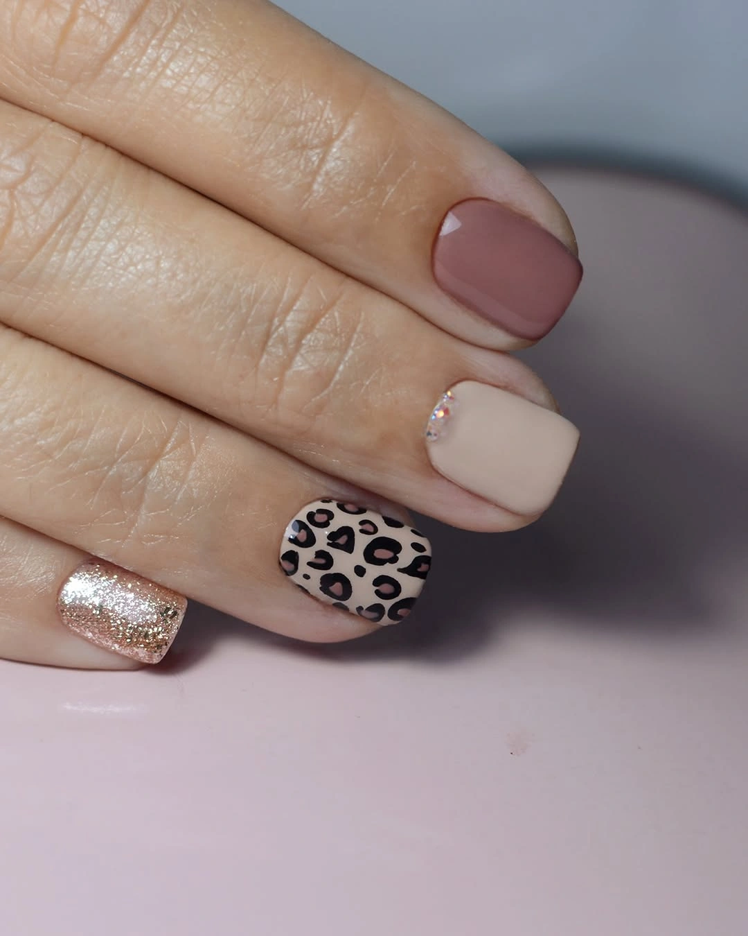 Short oval nude nails with taupe spots and glitter
