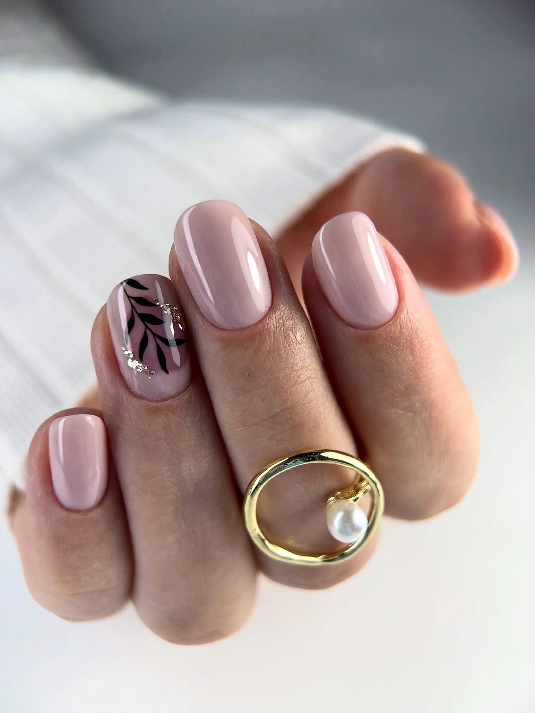 Short rounded pale pink nails with one black leafy accent