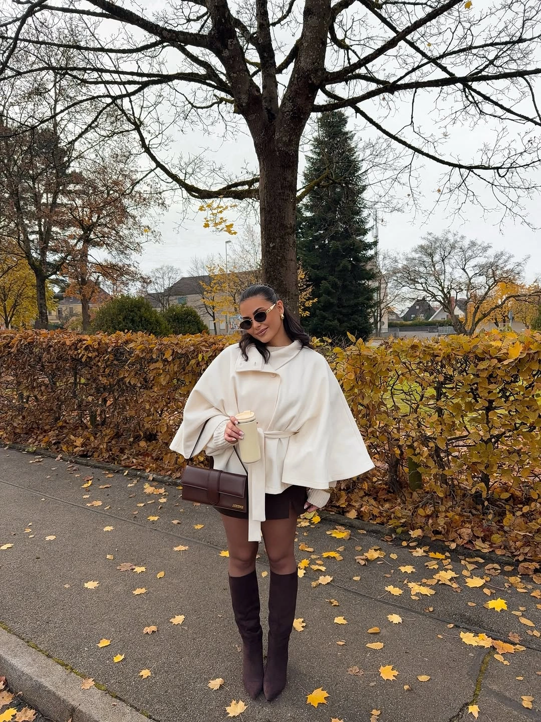 cream outfit with belted cape over short dark base with tall boots