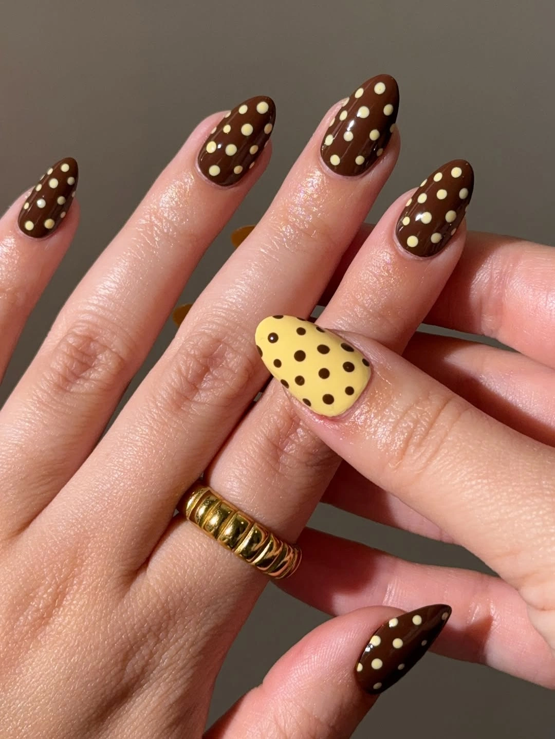 Brown dotted almond nails with one pale yellow accent