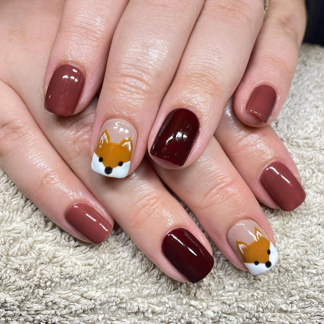 short rounded burgundy nails with tiny animal-like accents