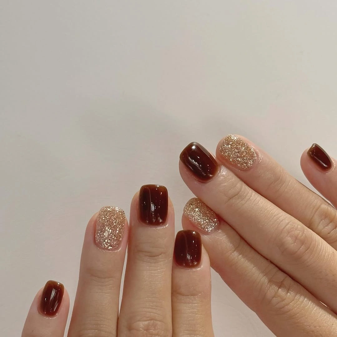 short rounded burgundy nails with pale gold glitter accents