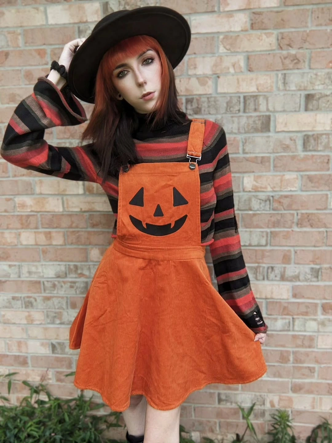 orange outfit with flared orange pinafore over striped top with wide hat