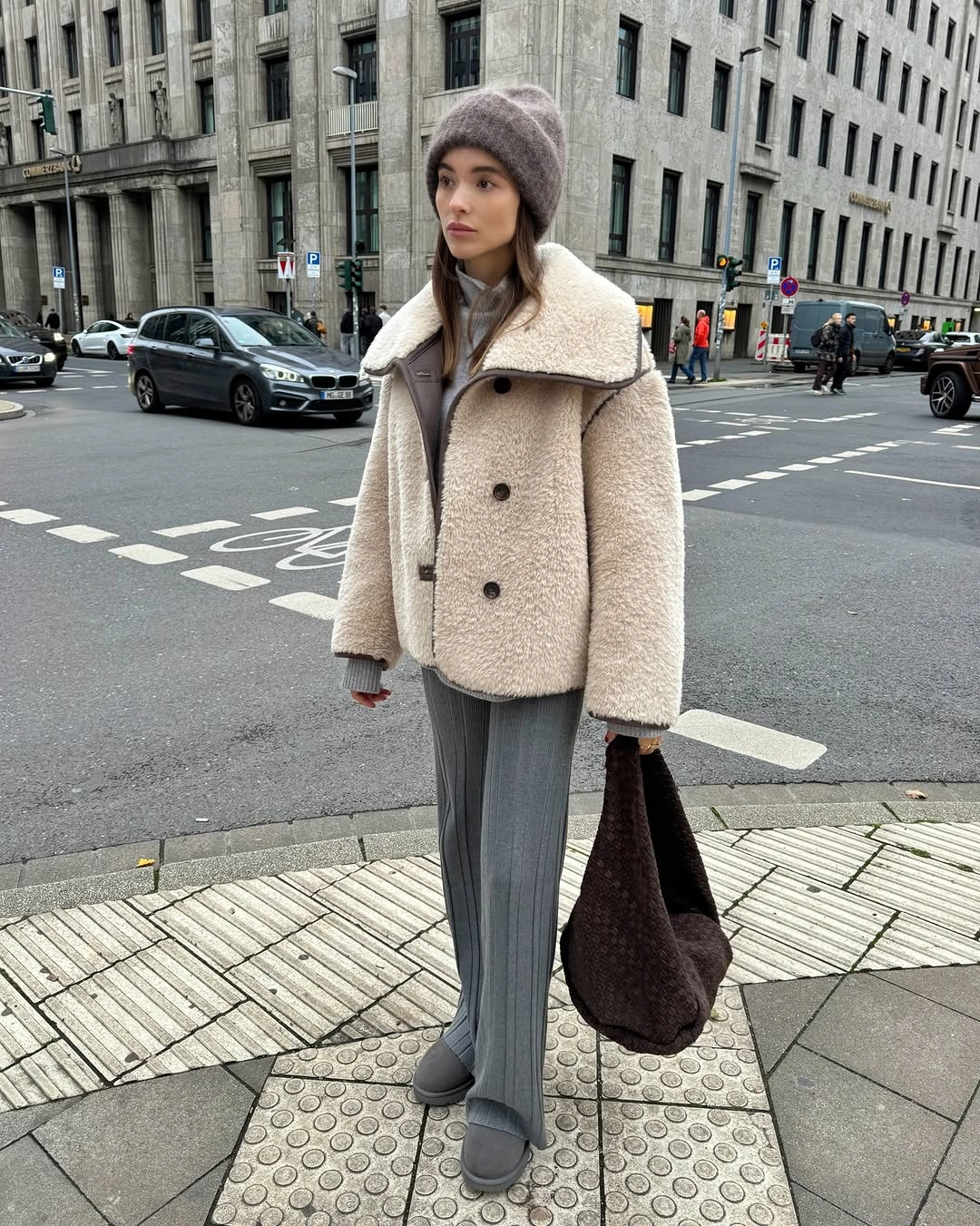 Cream fuzzy-looking coat with gray pants, beanie and dark bag
