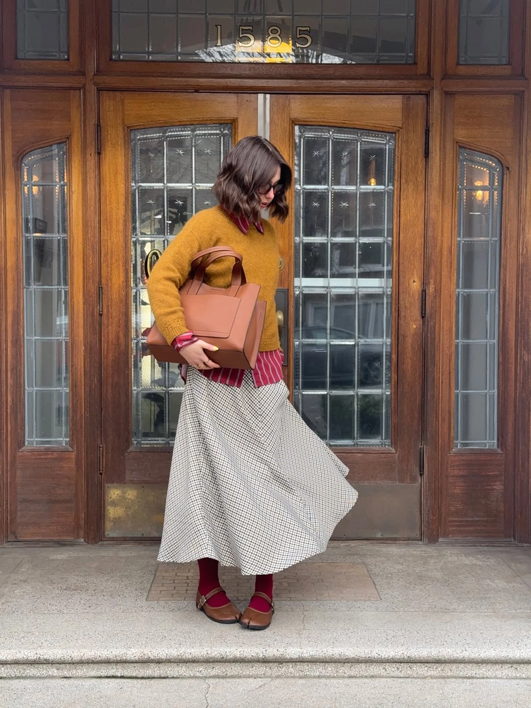 Mustard sweater, checked underlayer, grid midi skirt and tan tote