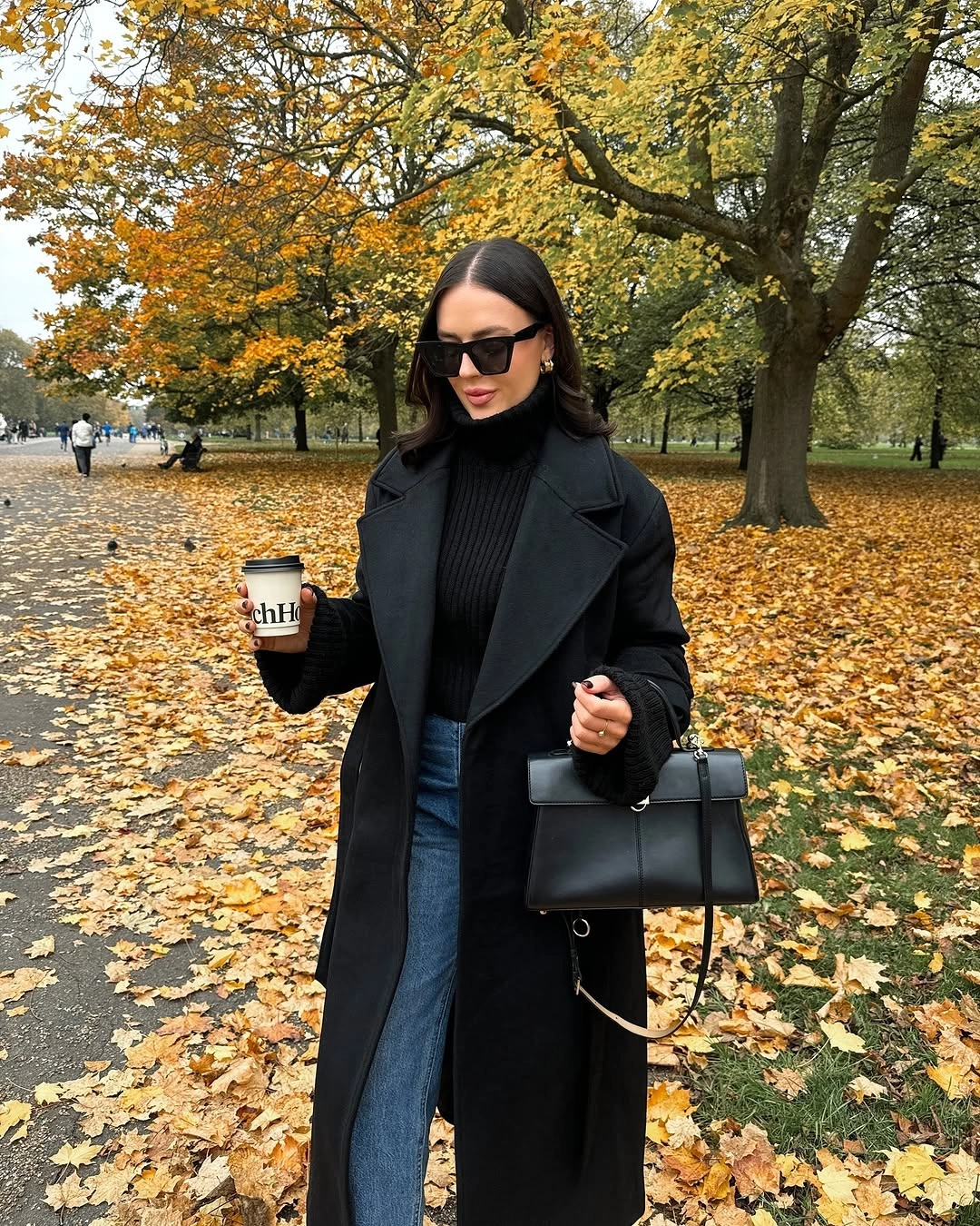 Long black coat, ribbed-looking sweater, blue jeans and structured handbag