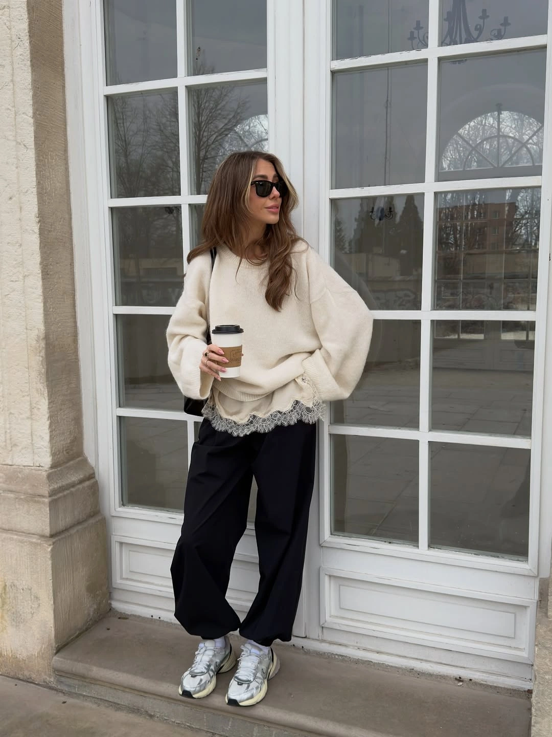 Cream oversized sweater with scalloped hem, black trousers, metallic sneakers