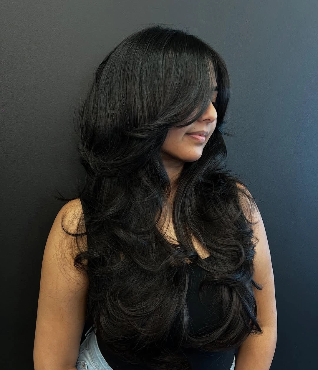 Long black side-swept haircut with cascading layers and curled ends