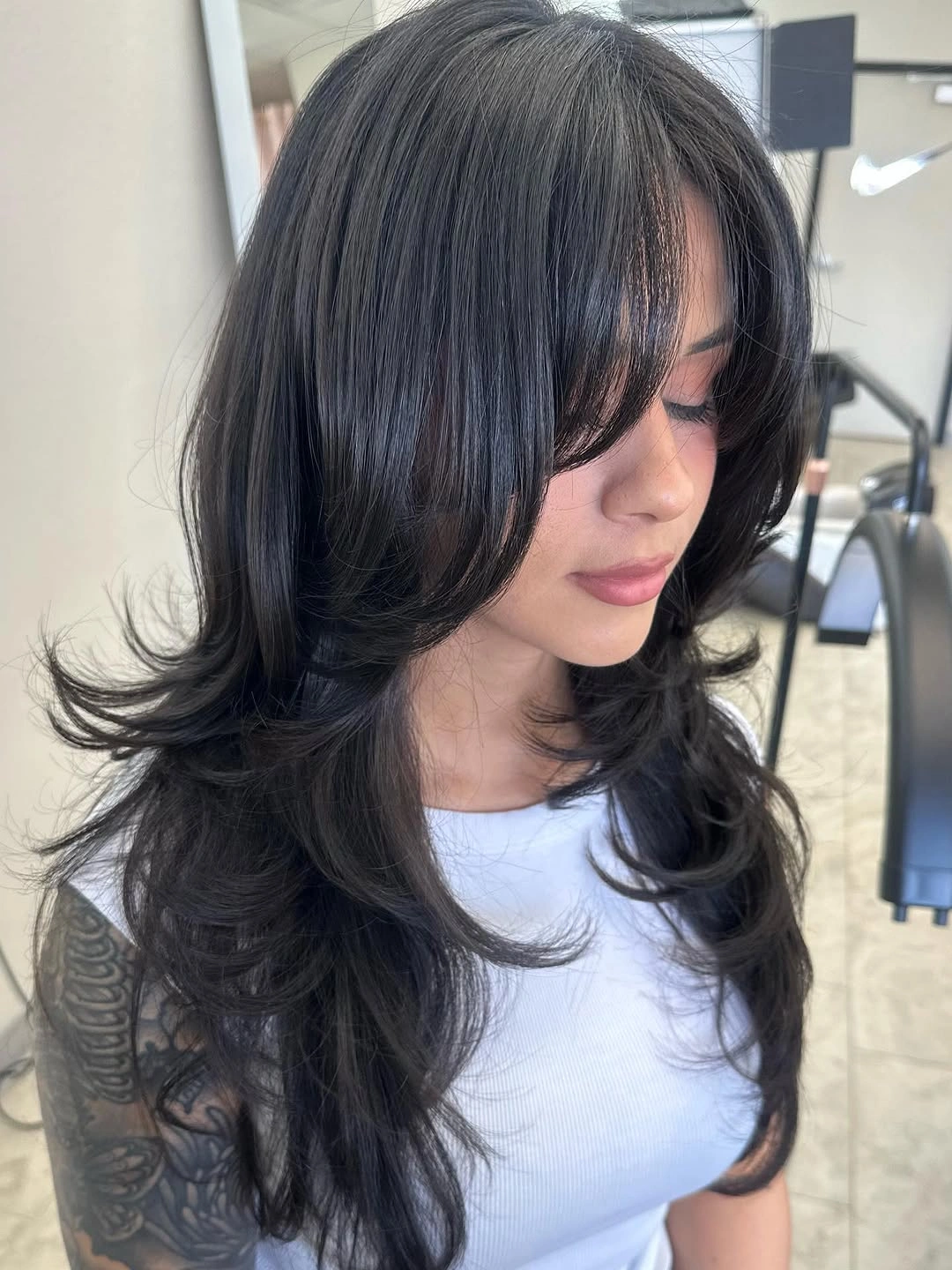 Long dark layered haircut with heavy curtain bangs and flipped ends