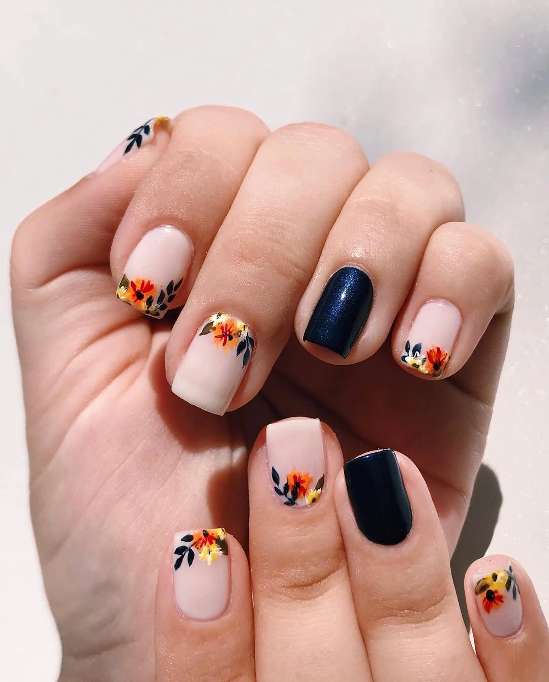 Short pale nails with orange florals and glossy navy accents