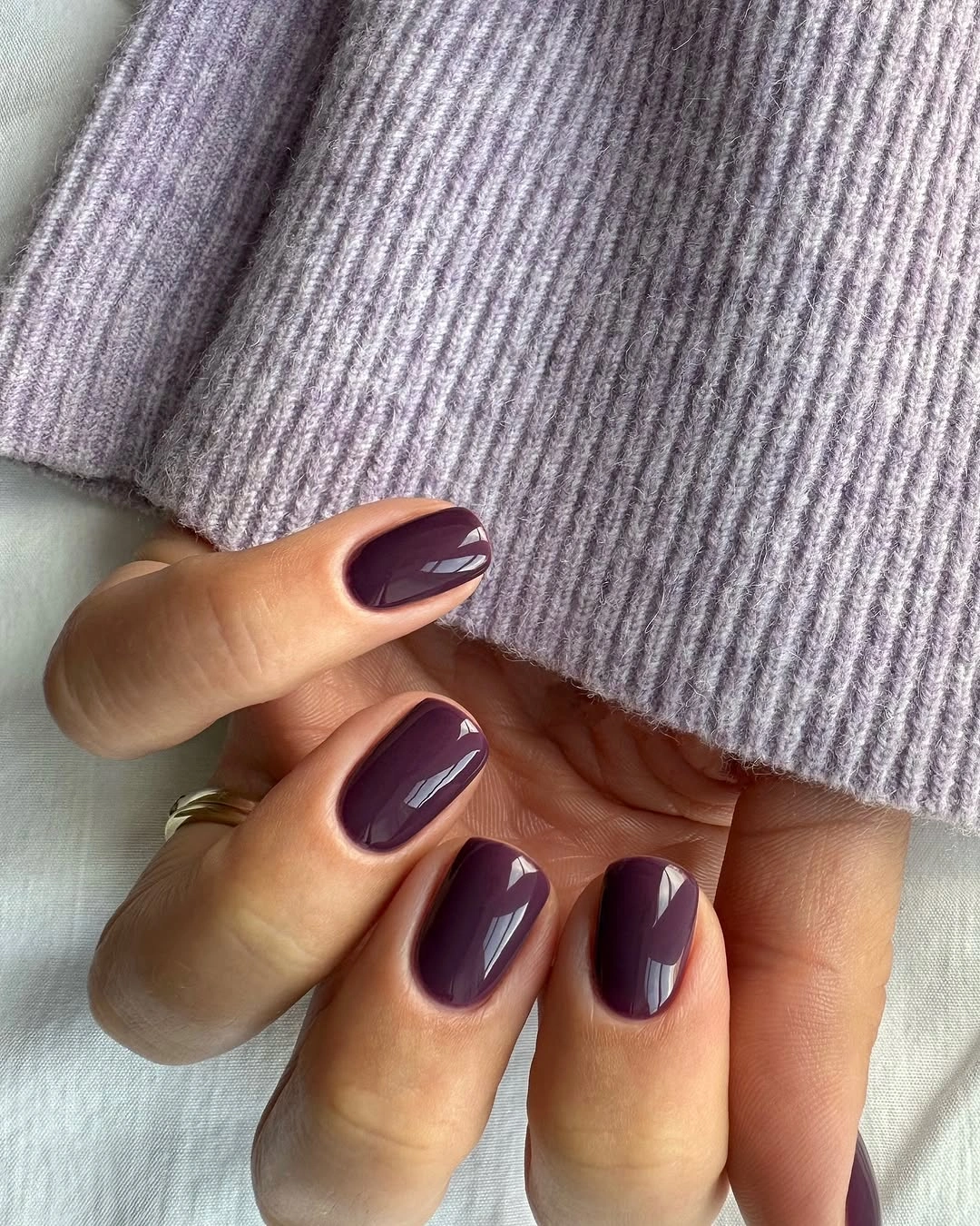Short glossy plum nails beside lilac ribbed knit