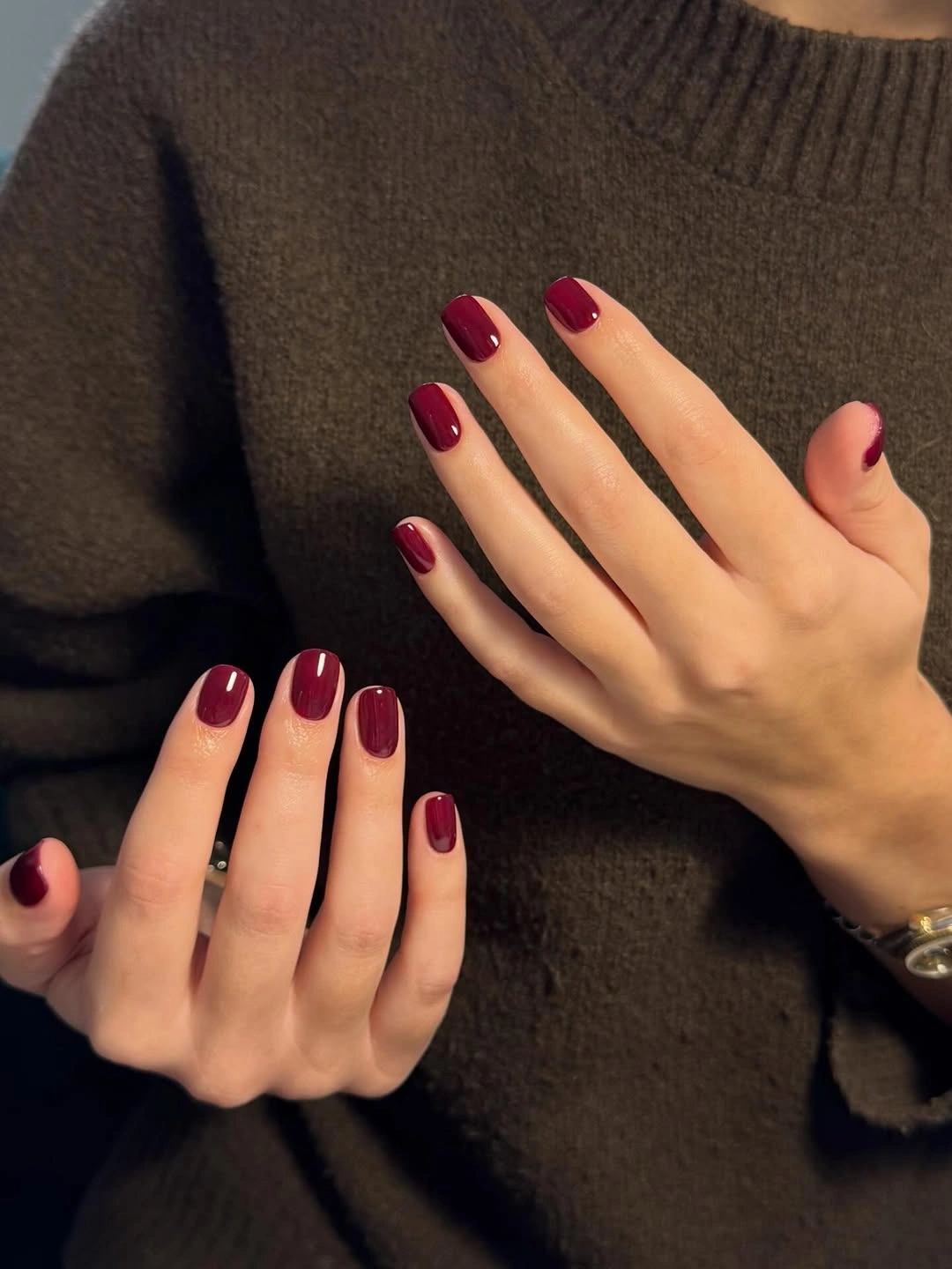 Glossy burgundy nails against a dark sweater