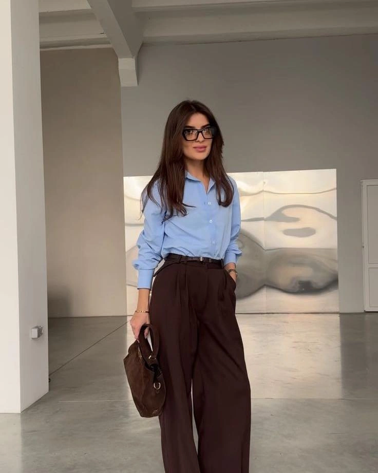 Light blue button-up shirt dark pleated trousers and brown bag