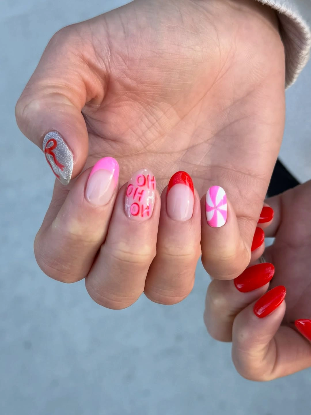 Short mismatched nails with red polish, pink lettering and peppermint swirl