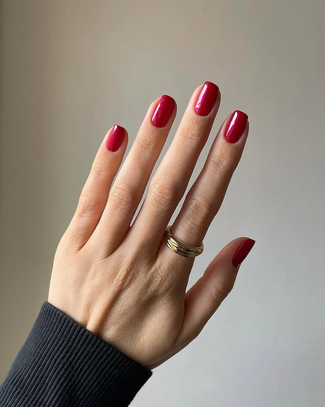 Short glossy red nails with rounded tips and dark sleeve