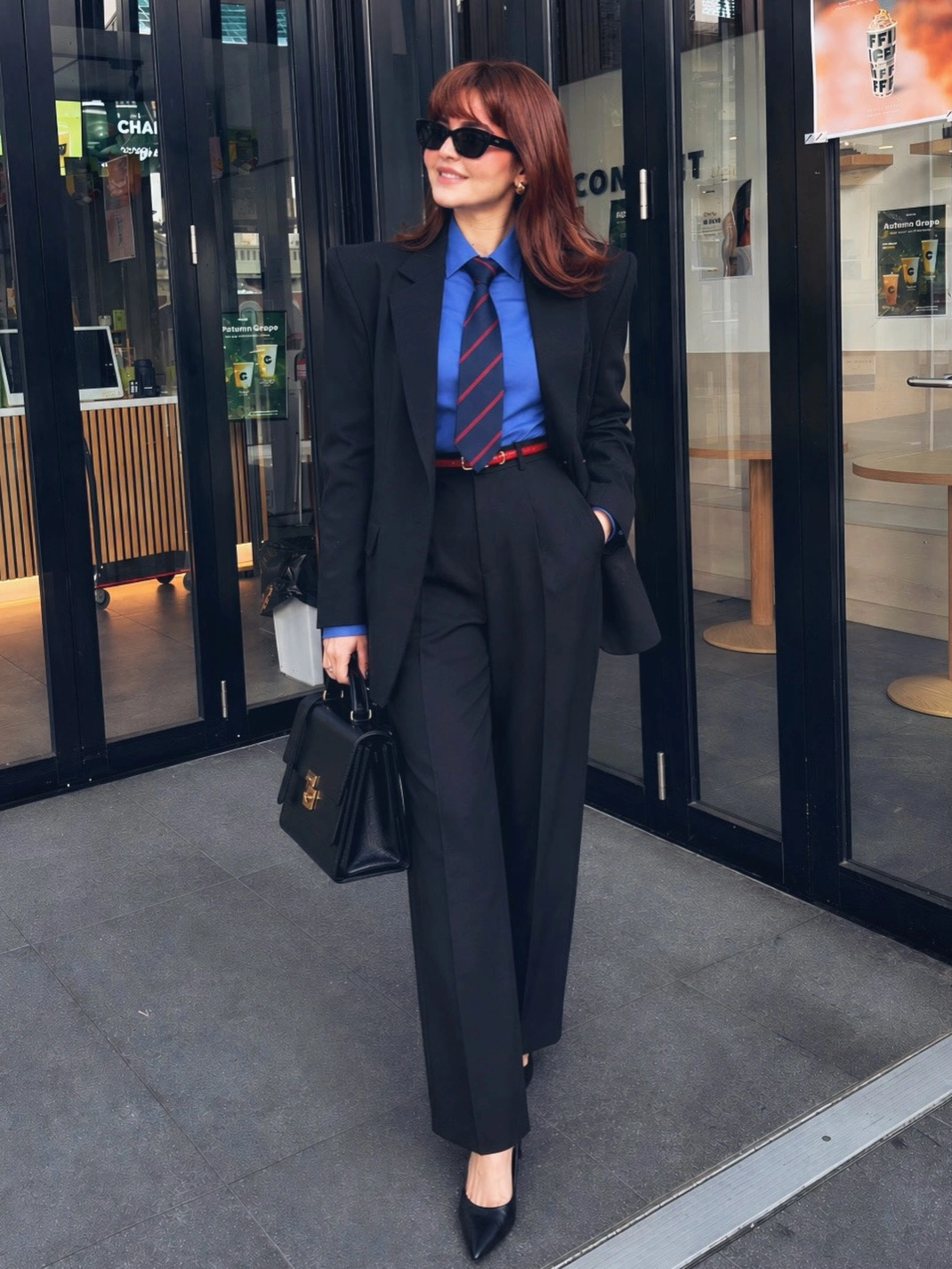 Dark suit bright blue shirt red striped tie and black handbag