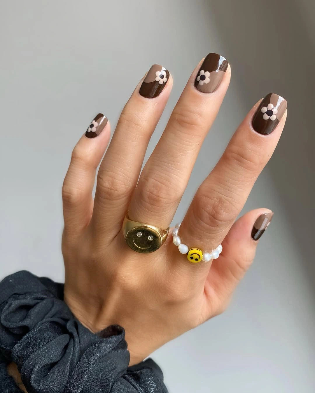 Short rounded nails with dark brown polish and white flowers