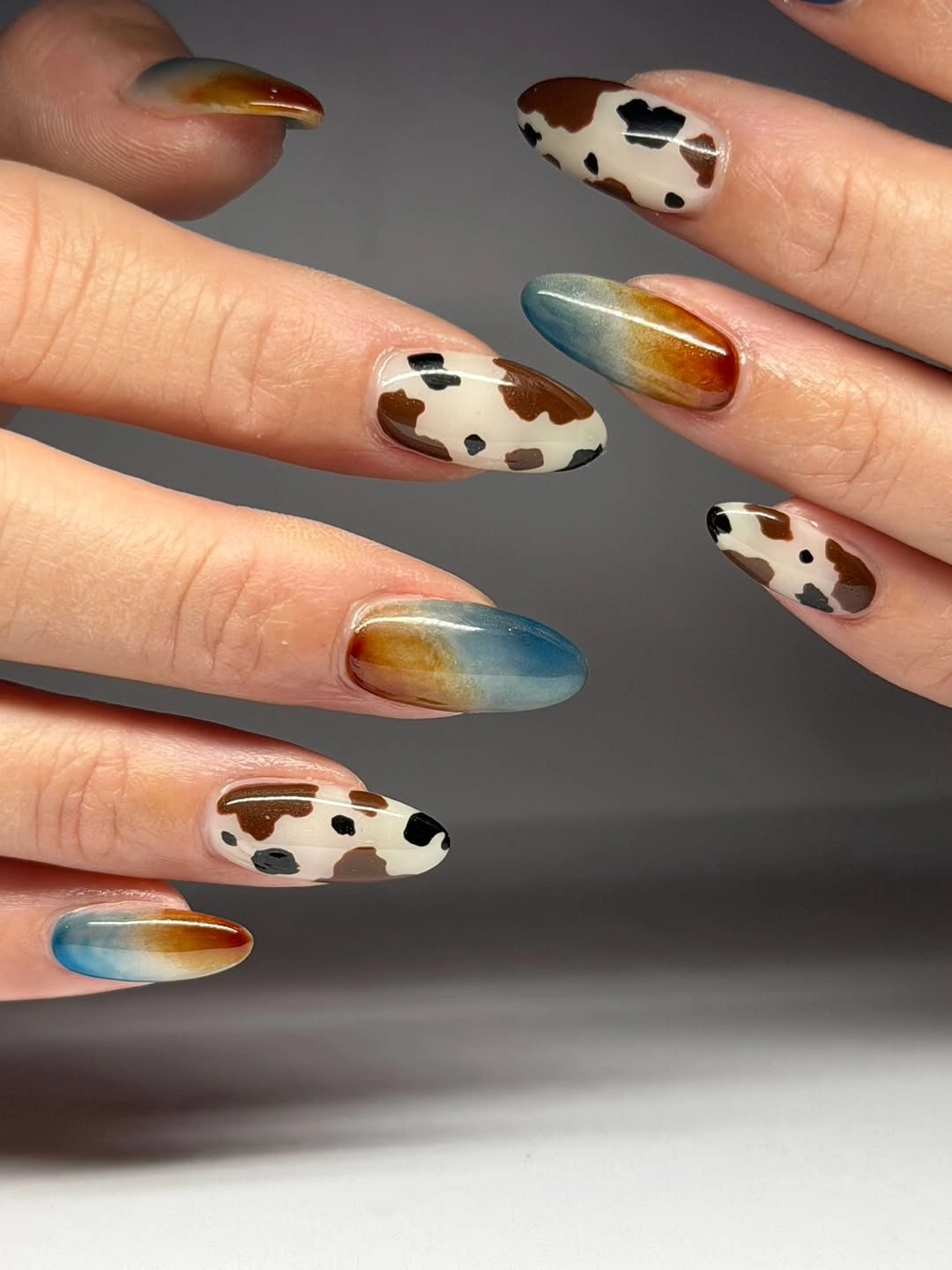 Almond nails with cow spots and glossy blue-to-rust gradients