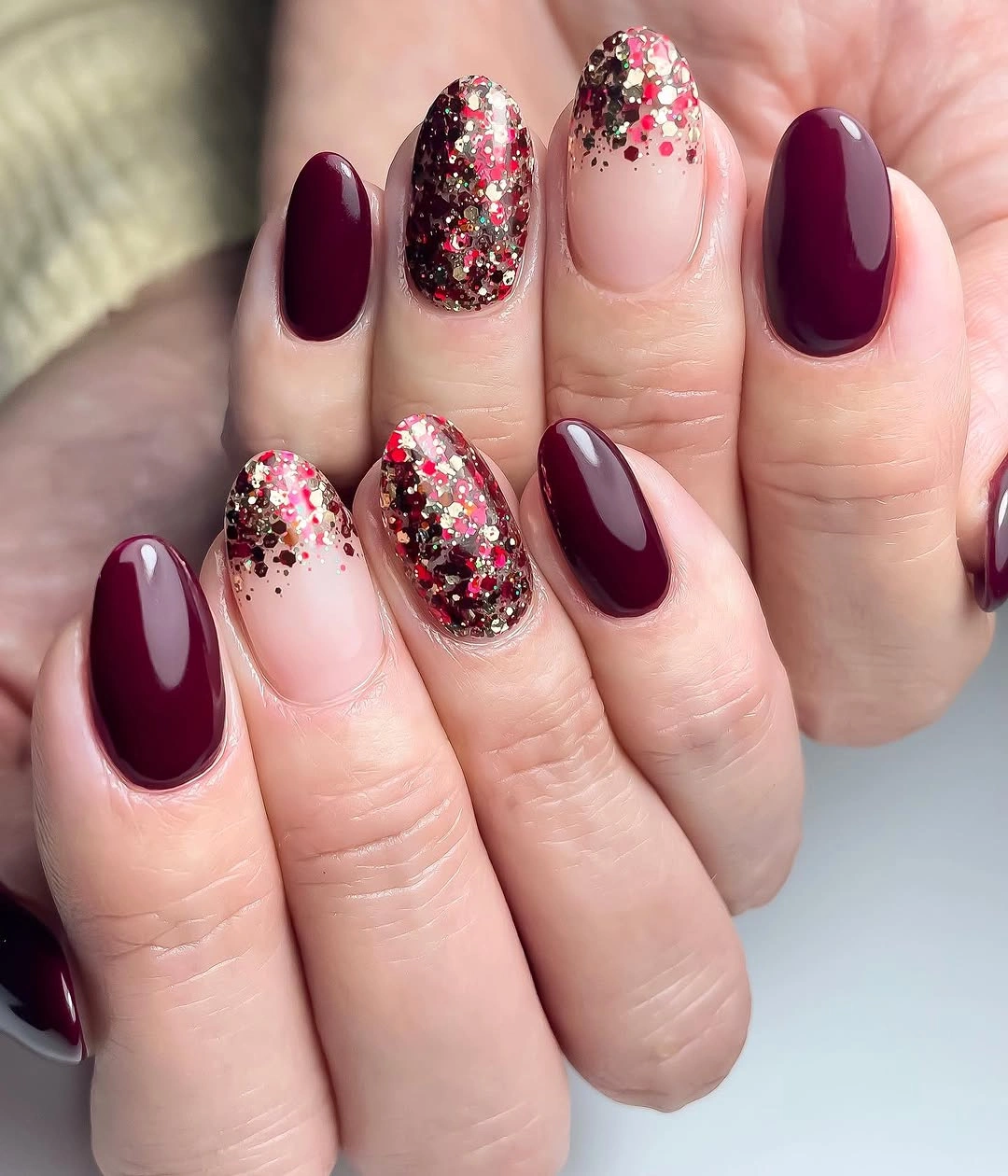 Short rounded burgundy nails with nude and glitter accents