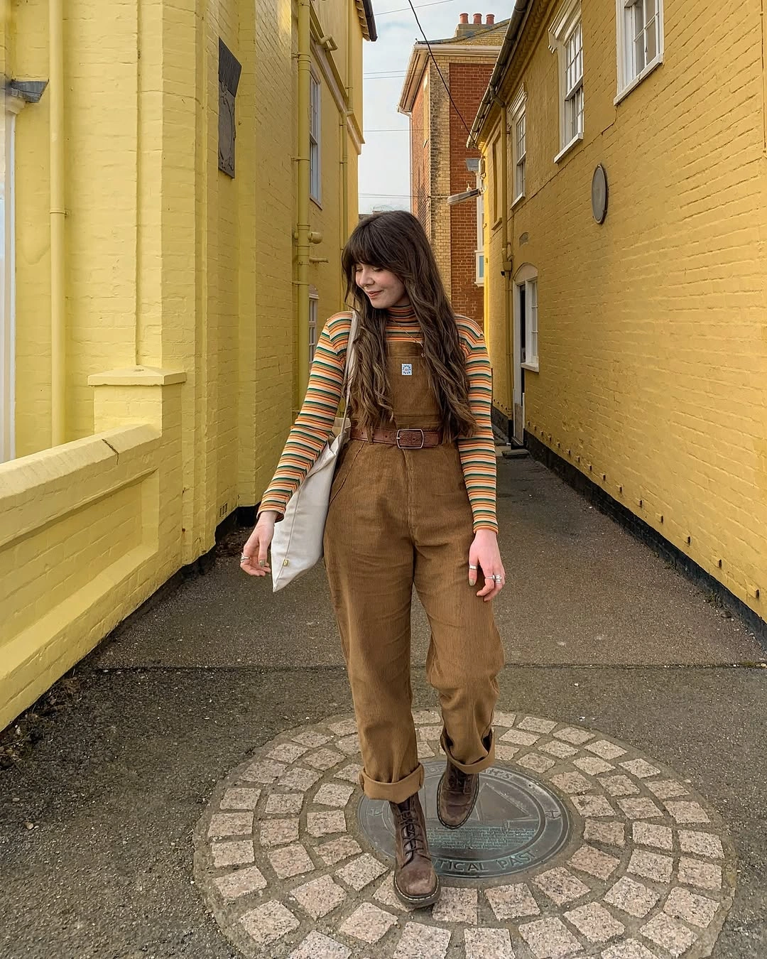Striped turtleneck under brown belted overalls with lace-up boots