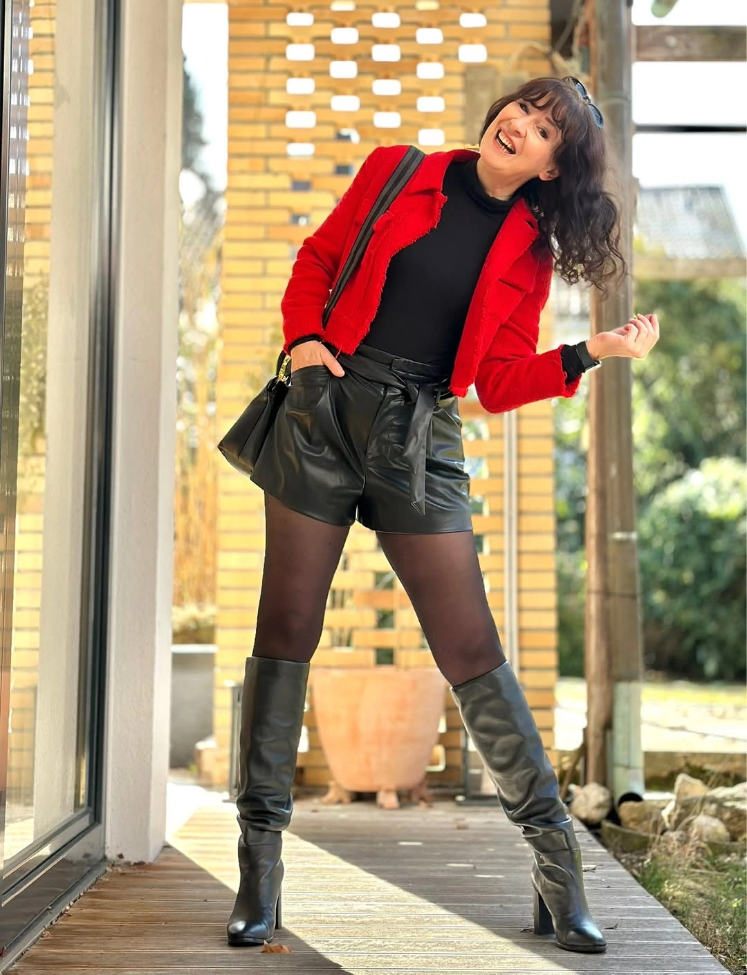 Woman wearing red jacket black shorts tights and tall boots