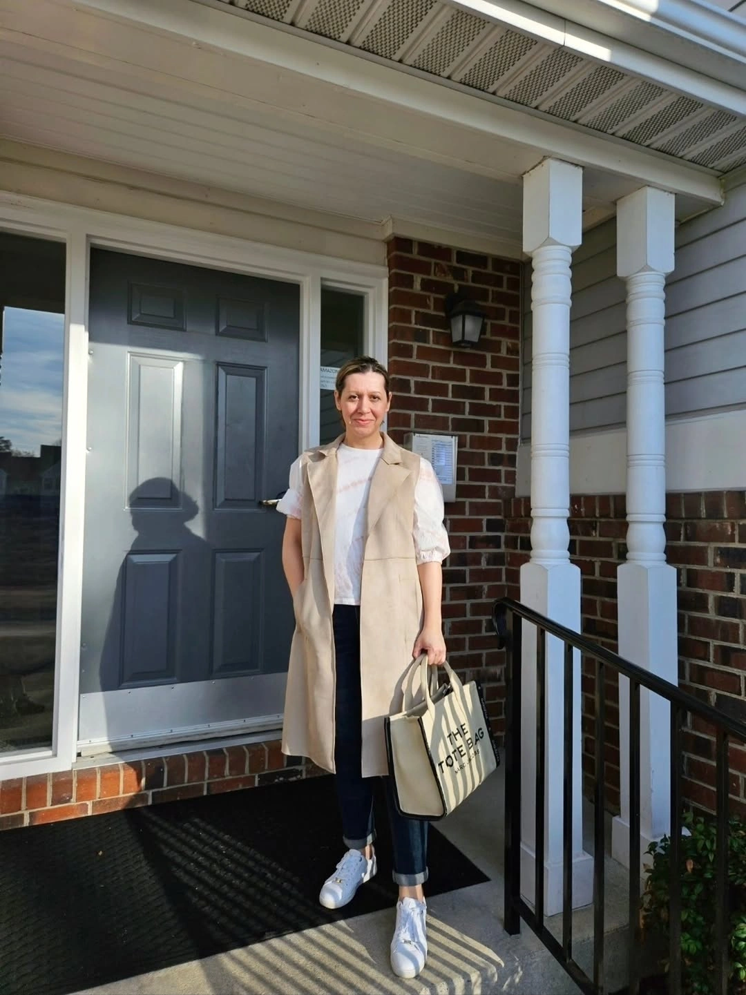 Woman in beige vest white top dark jeans and sneakers