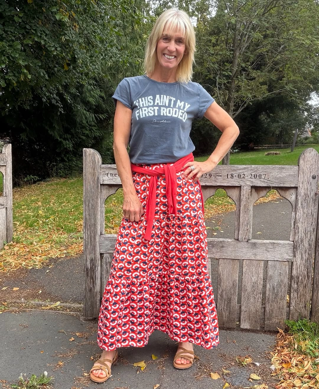 Woman in gray graphic tee red patterned skirt and sandals