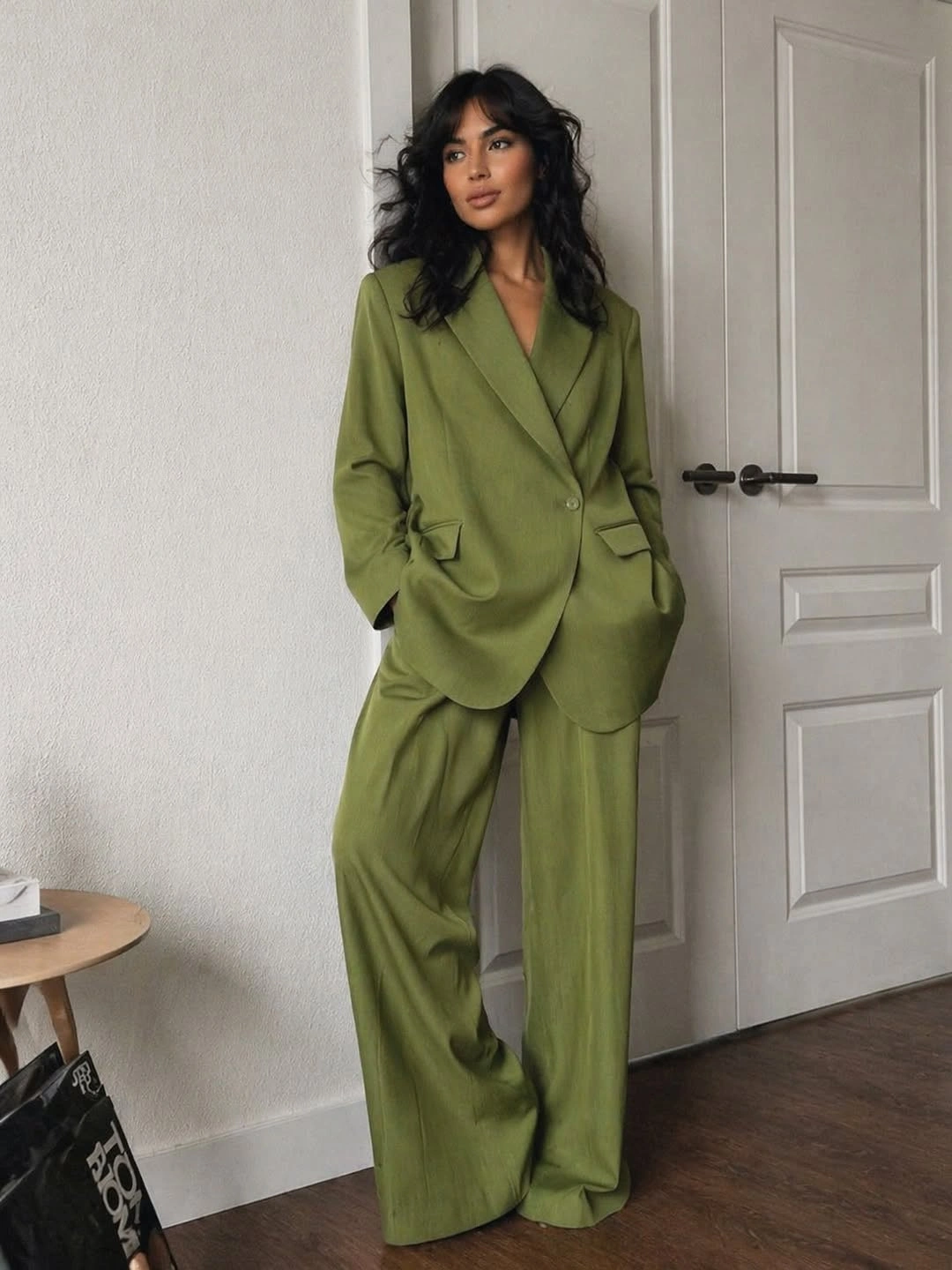 Woman in olive blazer and wide trousers indoors