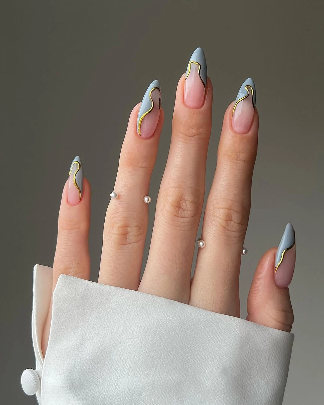 Pink almond nails with gray-blue tips and gold-colored wavy lines