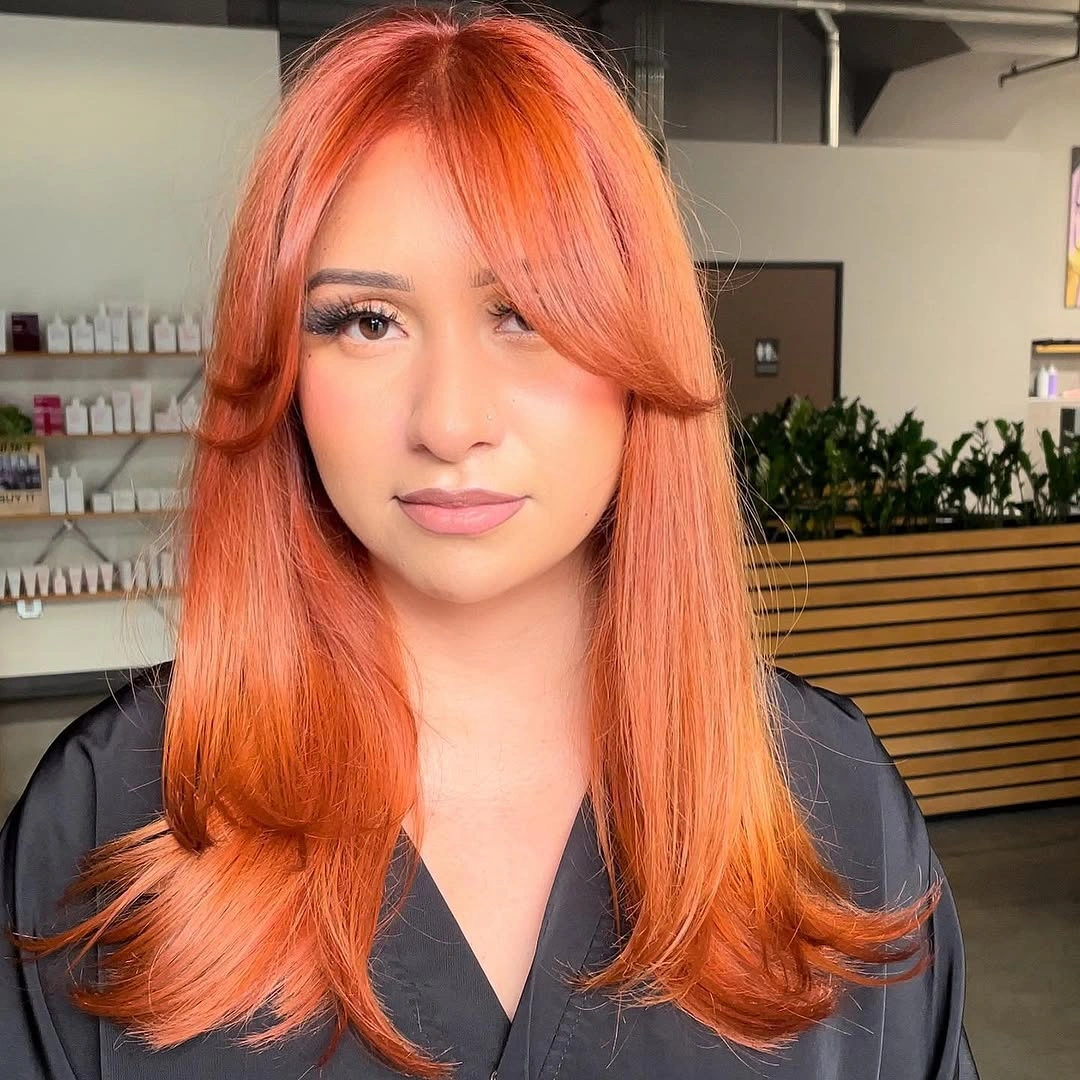 Long orange-coral layers with sweeping bangs and flipped ends
