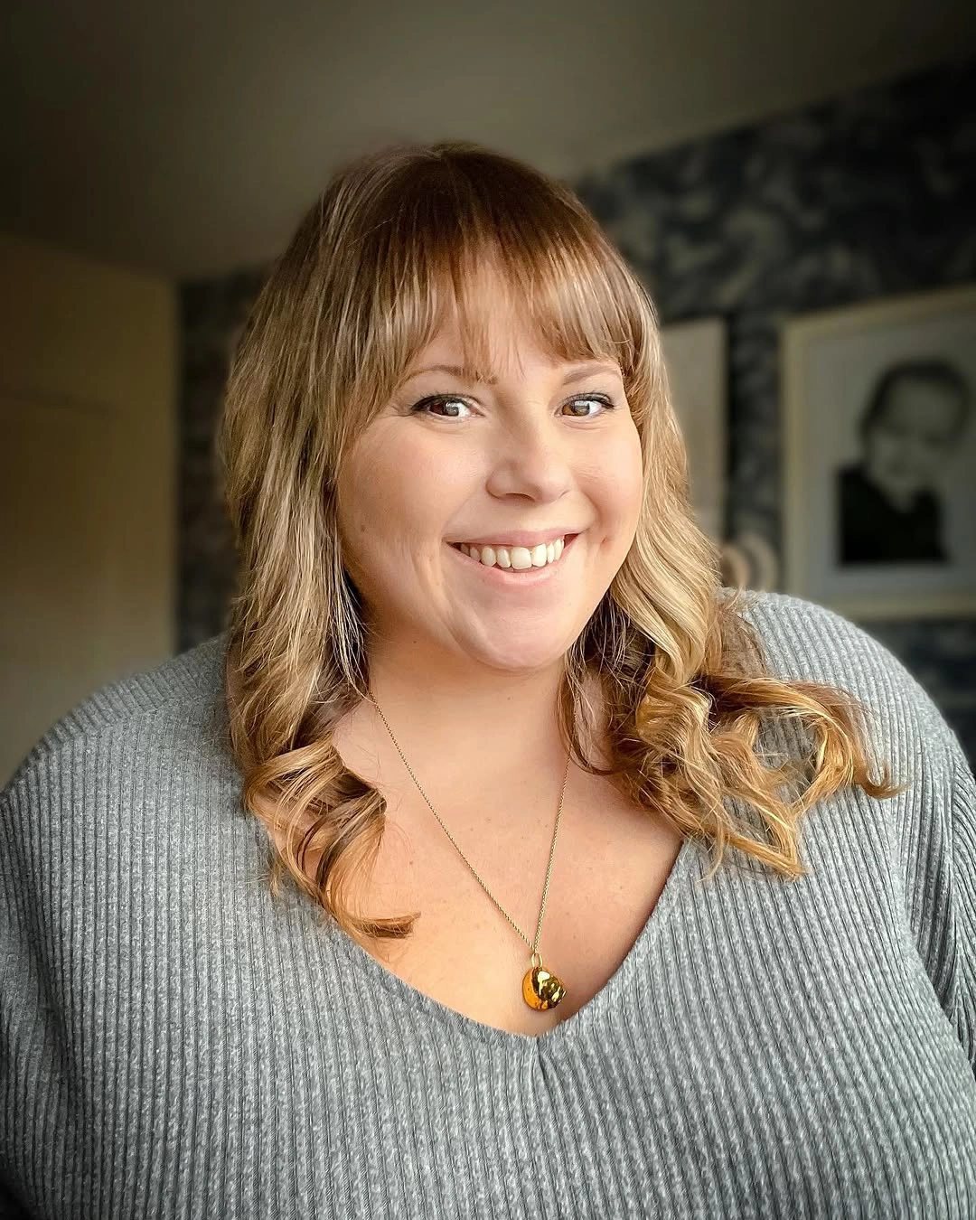 Blonde medium waves with full bangs and gray sweater