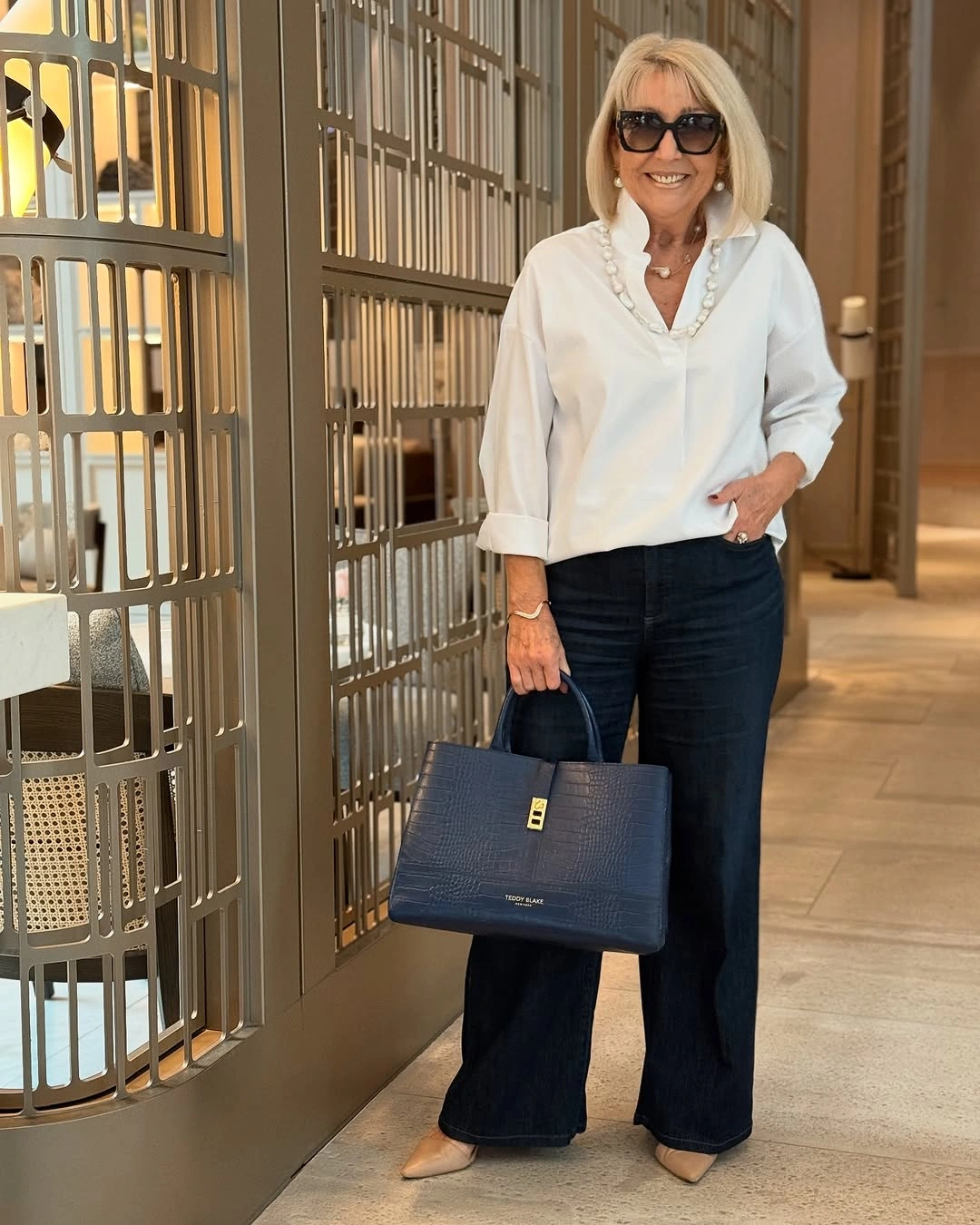 White blouse with dark wide jeans and navy handbag